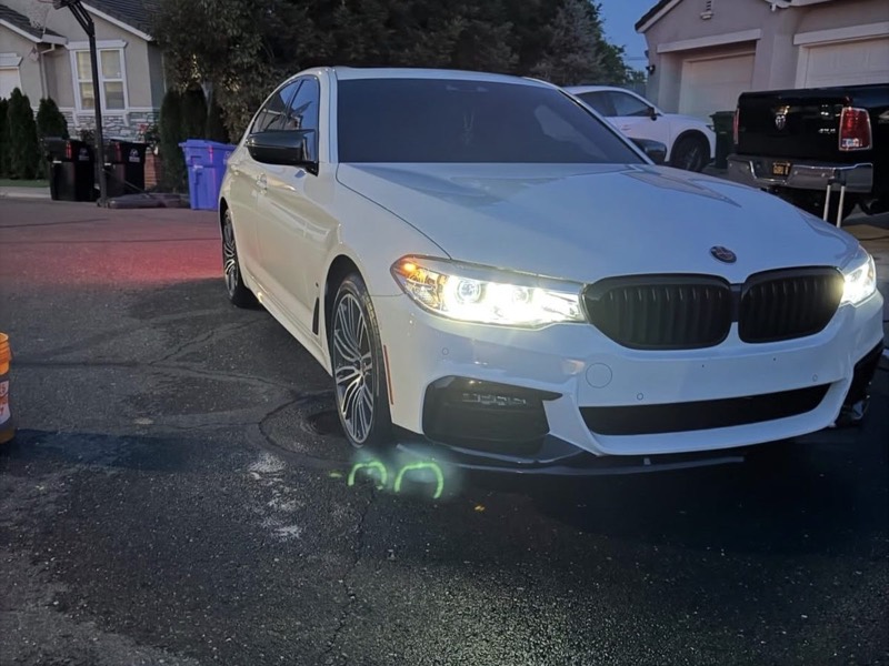 White BMW 540i with headlights on after a full detail